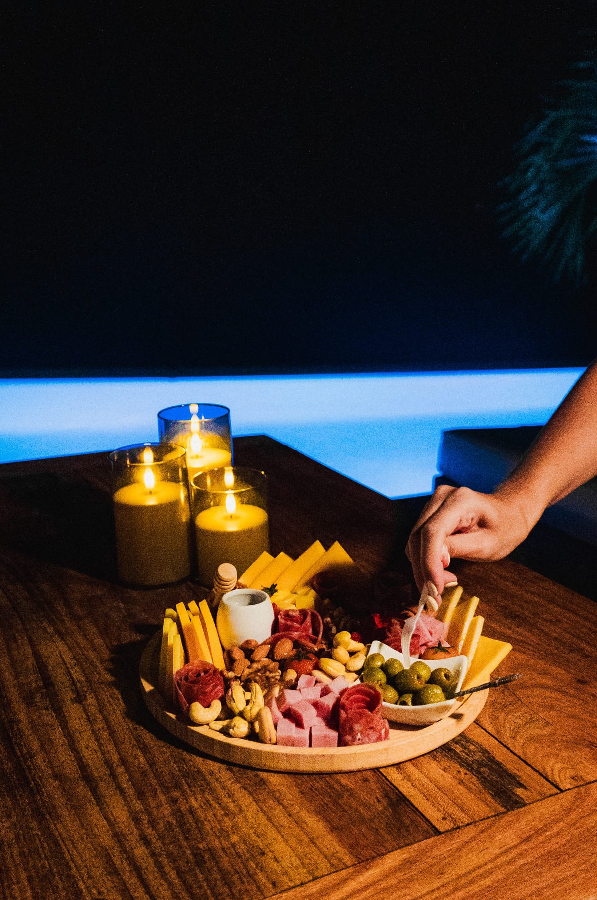 Tabla de charcutería junto a la piscina iluminada de noche